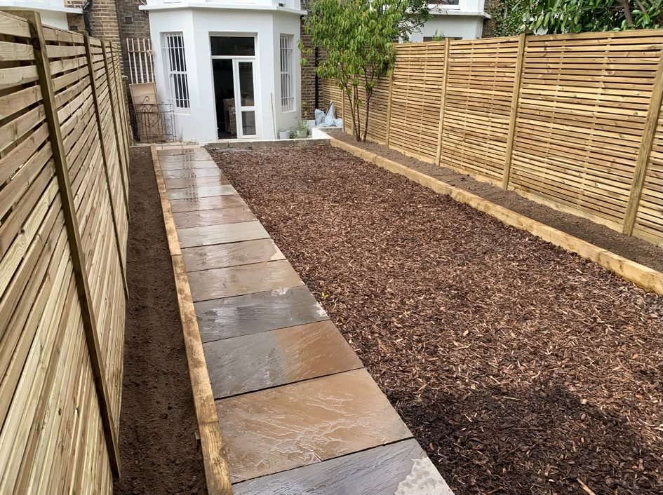 Slatted fencing along a long garden with a slab path and bark bed
